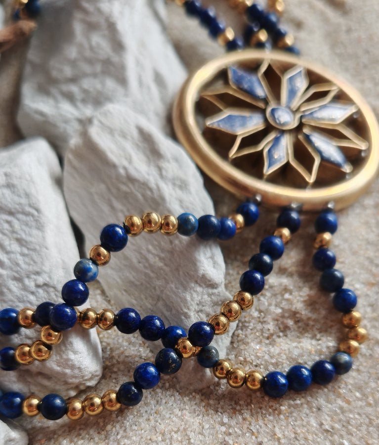 Beaded necklace with a decorative gold and blue pendant on a textured surface