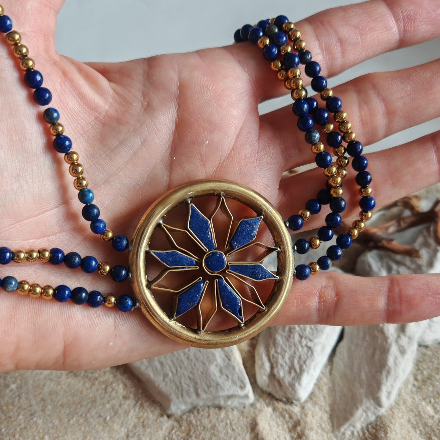 Necklace with a decorative sumerian pendant held in a hand on a sandy background